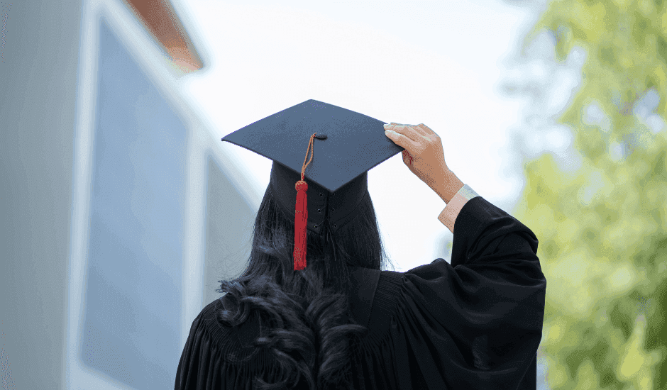 A newly qualified teacher in graduation cap and gown on a university campus, about to start their ECT induction
